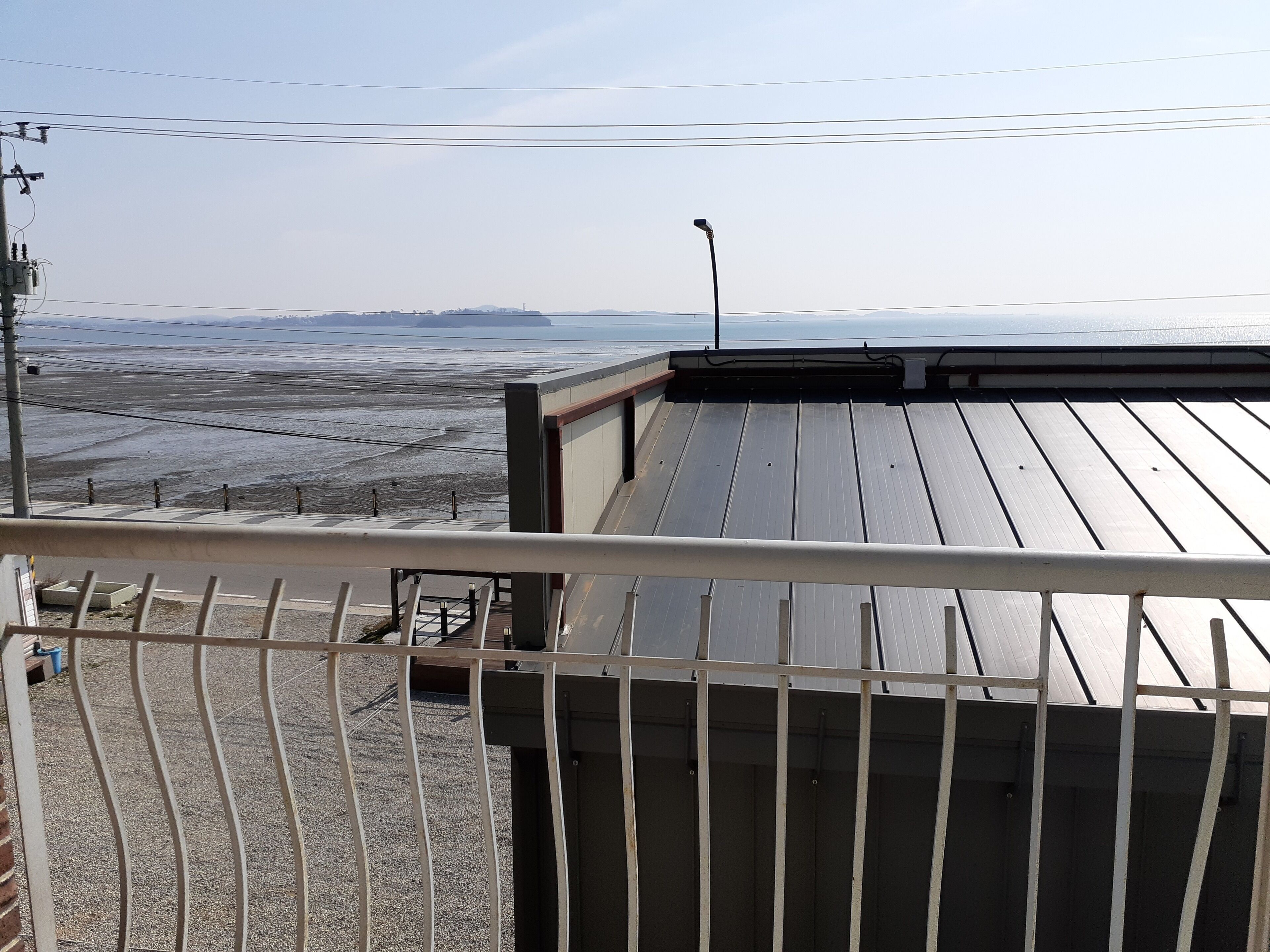 Una terraza en la azotea con barandilla metálica, vista a la playa y una cadena montañosa distante.