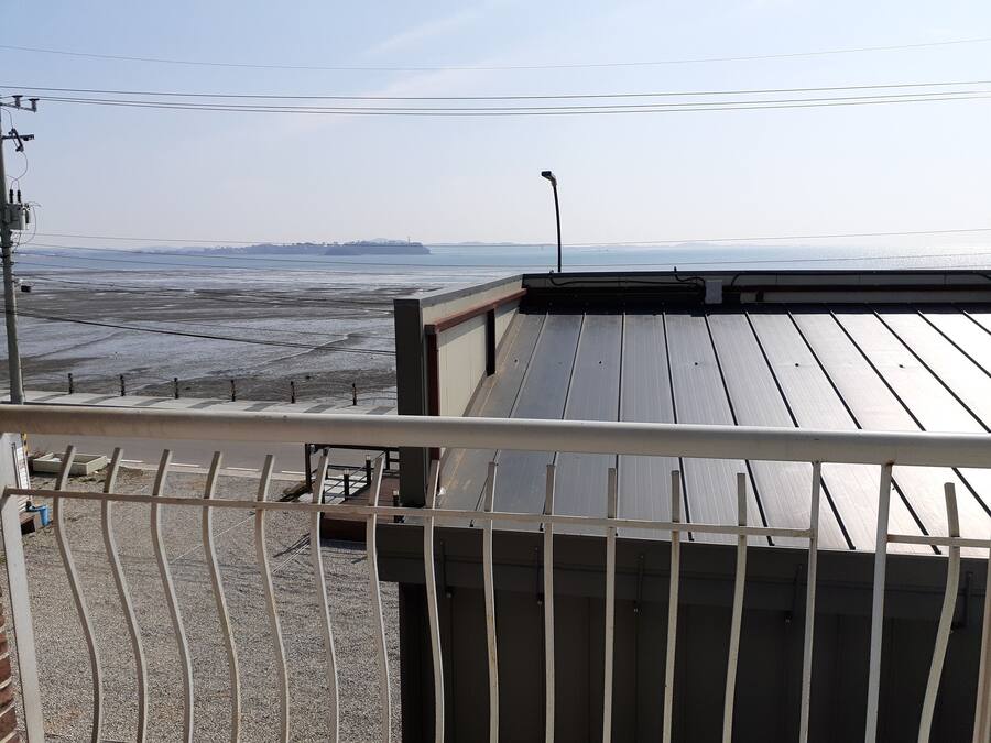 Una terraza en la azotea con barandilla metálica, vista a la playa y una cadena montañosa distante.