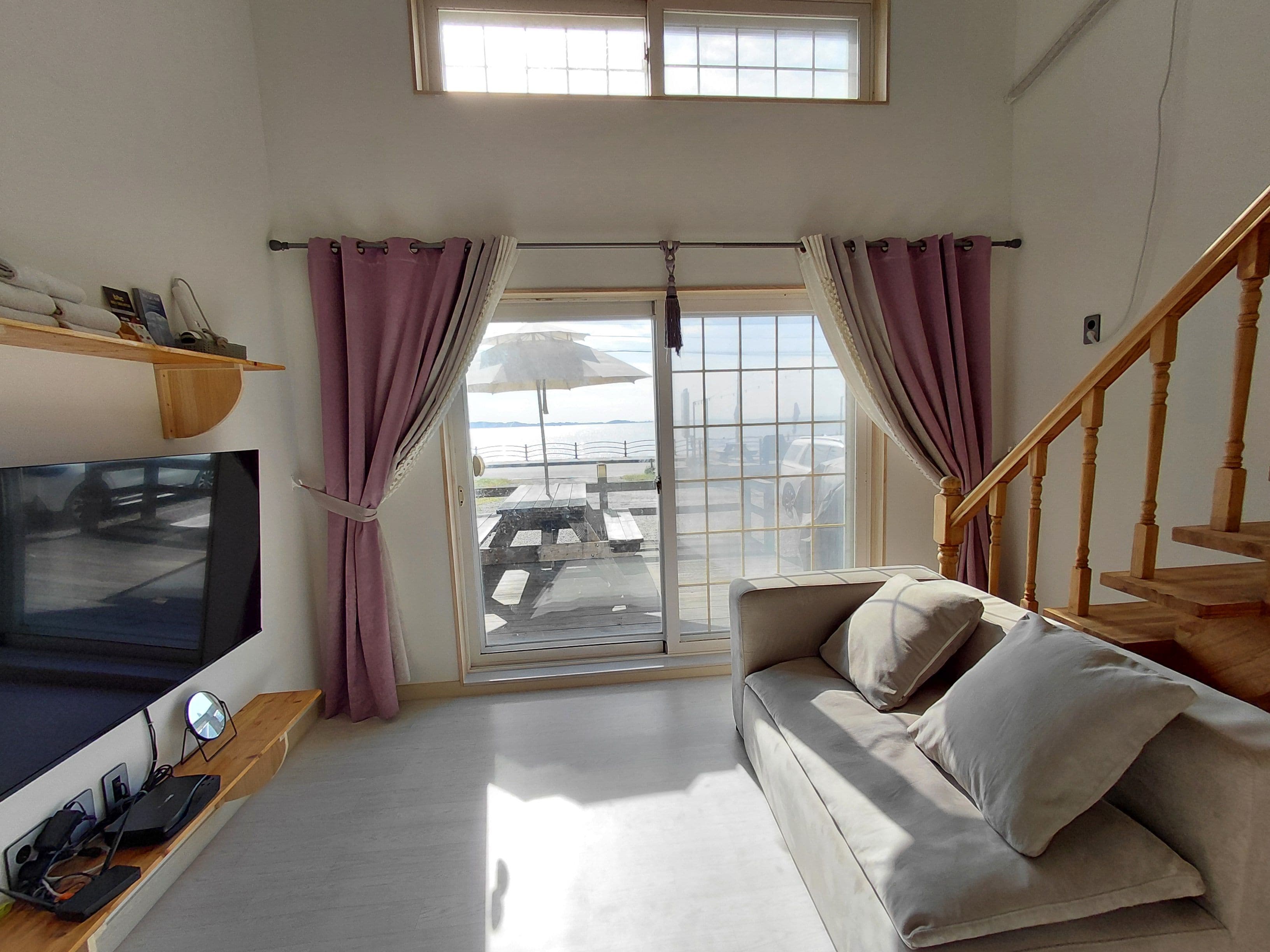 Ein Wohnzimmer mit einer Couch, einem Fernseher, einem Holzbodenregal und Blick durch eine Glastür.
