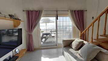 Ein Wohnzimmer mit einer Couch, einem Fernseher, einem Holzbodenregal und Blick durch eine Glastür.