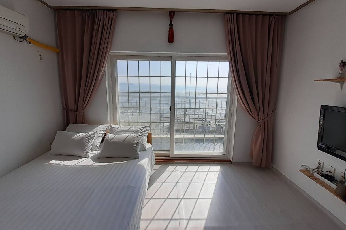 A bedroom with a bed, a TV, and a window with curtains.