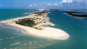 Eine Luftaufnahme einer Küstenregion mit sandigem Strand, klarem blauen Wasser und einer kleinen Insel mit Vegetation.