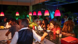 Eine Bar mit Sitzgelegenheiten, Tischen und einer Theke, an der verschiedene Gegenstände ausgestellt sind, ergänzt durch hängende Pendelleuchten.