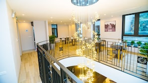 Ein modernes Interieur mit einer zentralen Treppe, einer hängenden Leuchte und einem Essbereich mit Tischen und Stühlen.