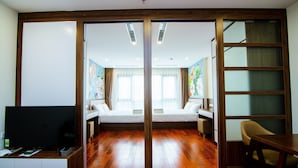 Ein Hotelzimmer mit Holzboden, Fernseher, Schreibtisch und einem Bett mit Blick auf die Stadt durch große Fenster.