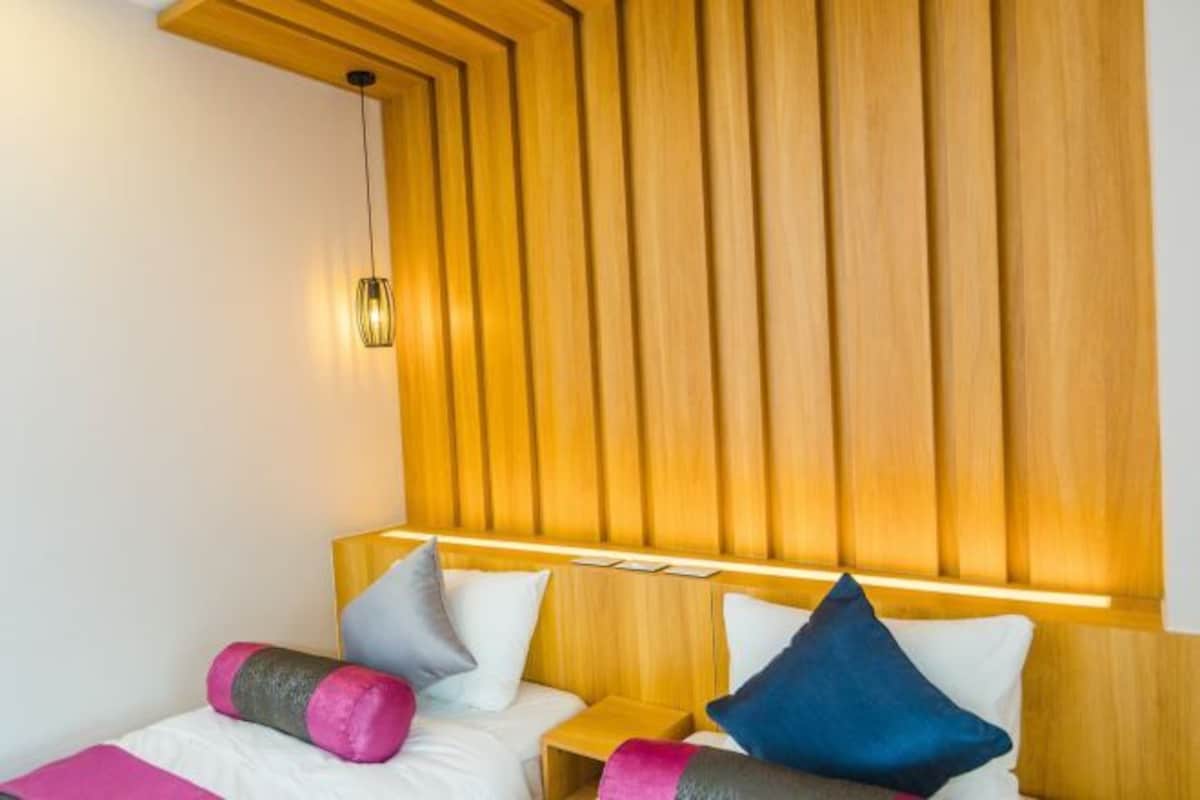 Habitación de hotel con dos camas, cabecero de madera y una lámpara fijada a la pared.