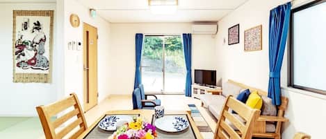 A modern living room with a dining table, chairs, a sofa, and a TV.