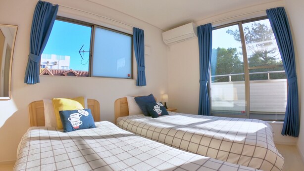 Ein Hotelzimmer mit zwei Betten, einem Fenster mit Vorhängen, einer Klimaanlage und Blick nach draußen.