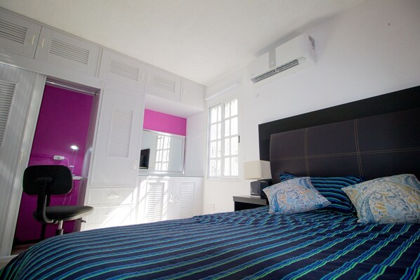 Un dormitorio con cama, una silla, un escritorio y una ventana.