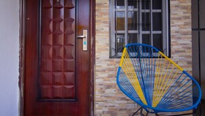 A wooden door with geometric patterns, a blue and yellow chair, and a window with metal bars. - Casa Zac Nicte Mx ROOM IXCHEL (CANCUN)