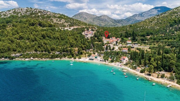 Eine Vogelperspektive einer Küstenstadt mit klarem türkisblauem Meer, umgeben von grünen Hügeln und Bergen.