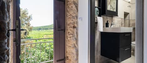 Un baño de diseño moderno, con un espejo grande y vistas a un viñedo a través de una puerta abierta.