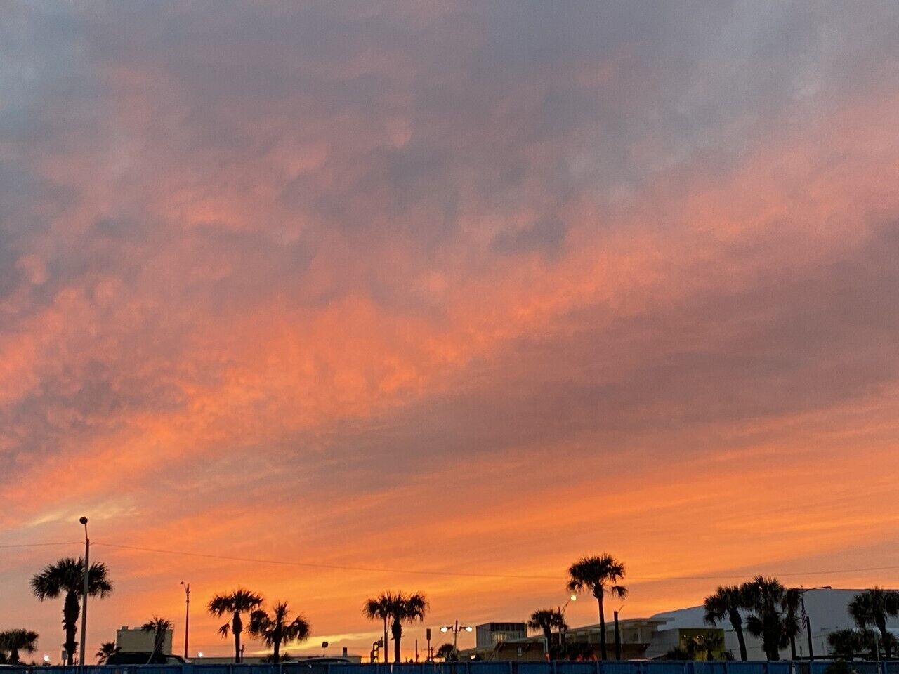Un ciel au coucher du soleil, avec des palmiers et des bâtiments au premier plan.