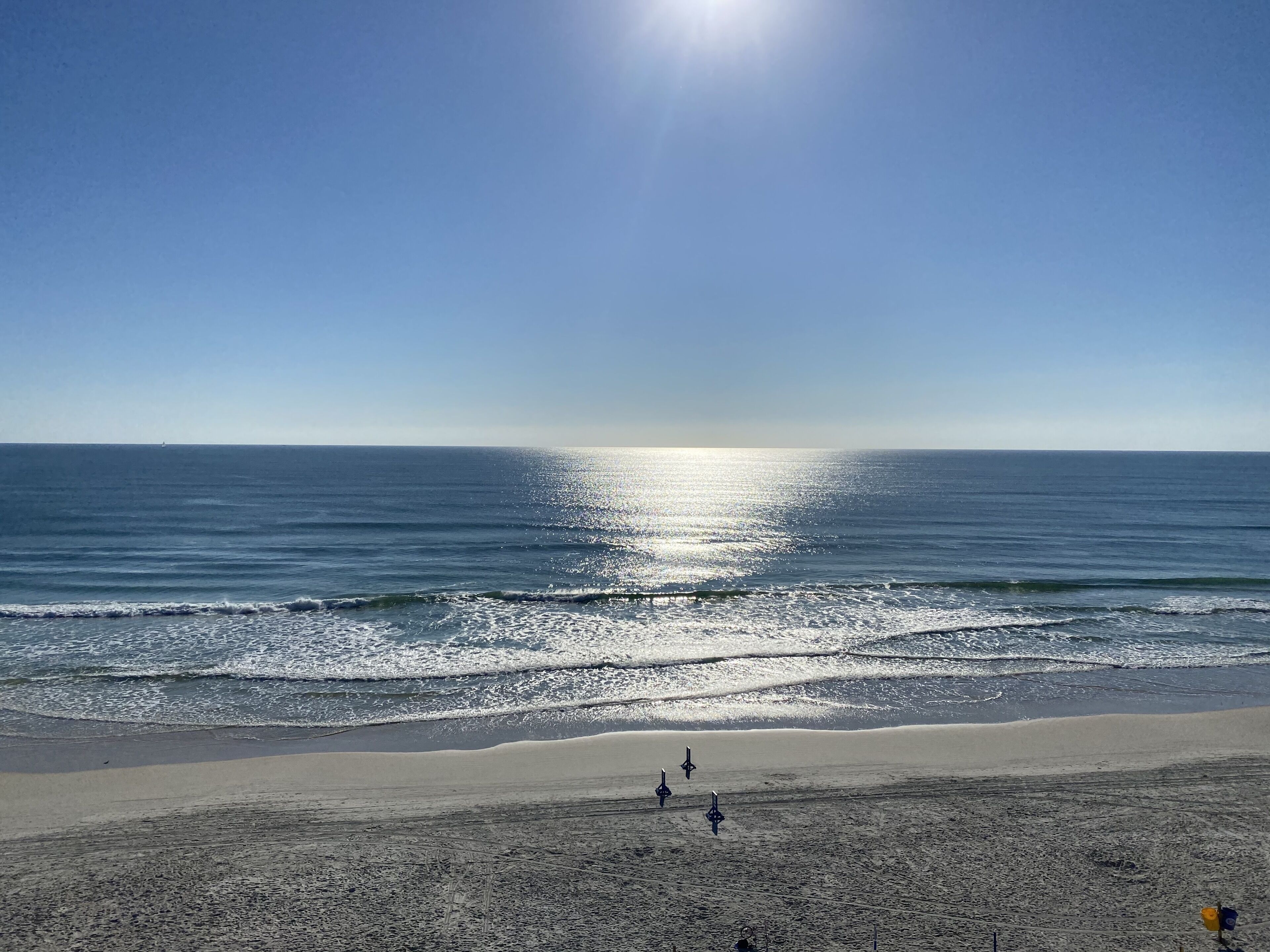 Una playa con cielo despejado, mar tranquilo y algunas personas a lo lejos.