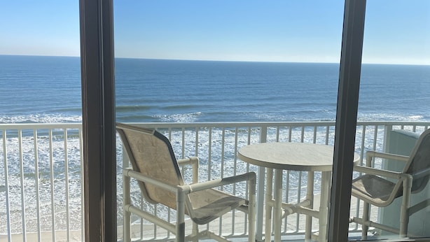 A balcony with a table and chairs overlooking the ocean.