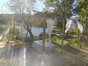 A covered outdoor seating area with tables and chairs, a pergola, and a view of a lake. - COTTAGE Nº2 AT THE FOOT OF THE LAGOON (Ruidera)