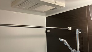 A modern bathroom with a glass shower enclosure, a visible ventilation system, and a sleek, dark-colored wall. - JR Komagome Apartment 1-1 (Tokyo)