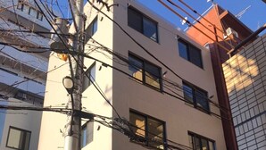 A multi-story building with a flat facade, multiple windows, and visible electrical wires. - JR Komagome Apartment 1-1 (Tokyo)