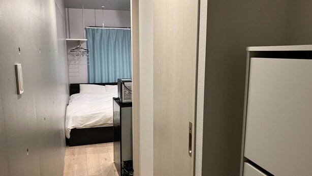 A narrow hallway leading to a bedroom with a bed, a desk, and a wardrobe. - JR Komagome Apartment 1-1 (Tokyo)