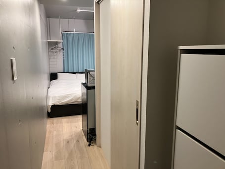 A narrow hallway leading to a bedroom with a bed, a desk, and a wardrobe.