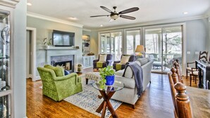 A spacious living room with a fireplace, green armchairs, a sofa, and a dining area with wooden chairs. - 5 Bedroom renovated Home in Great Waters at Reynolds Lake Oconee (Eatonton)