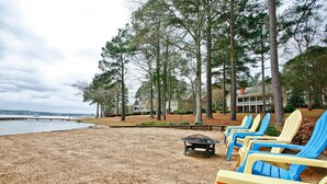 A beach with blue and yellow Adirondack chairs, a fire pit, and a view of the water and trees. - 5 Bedroom renovated Home in Great Waters at Reynolds Lake Oconee (Eatonton)
