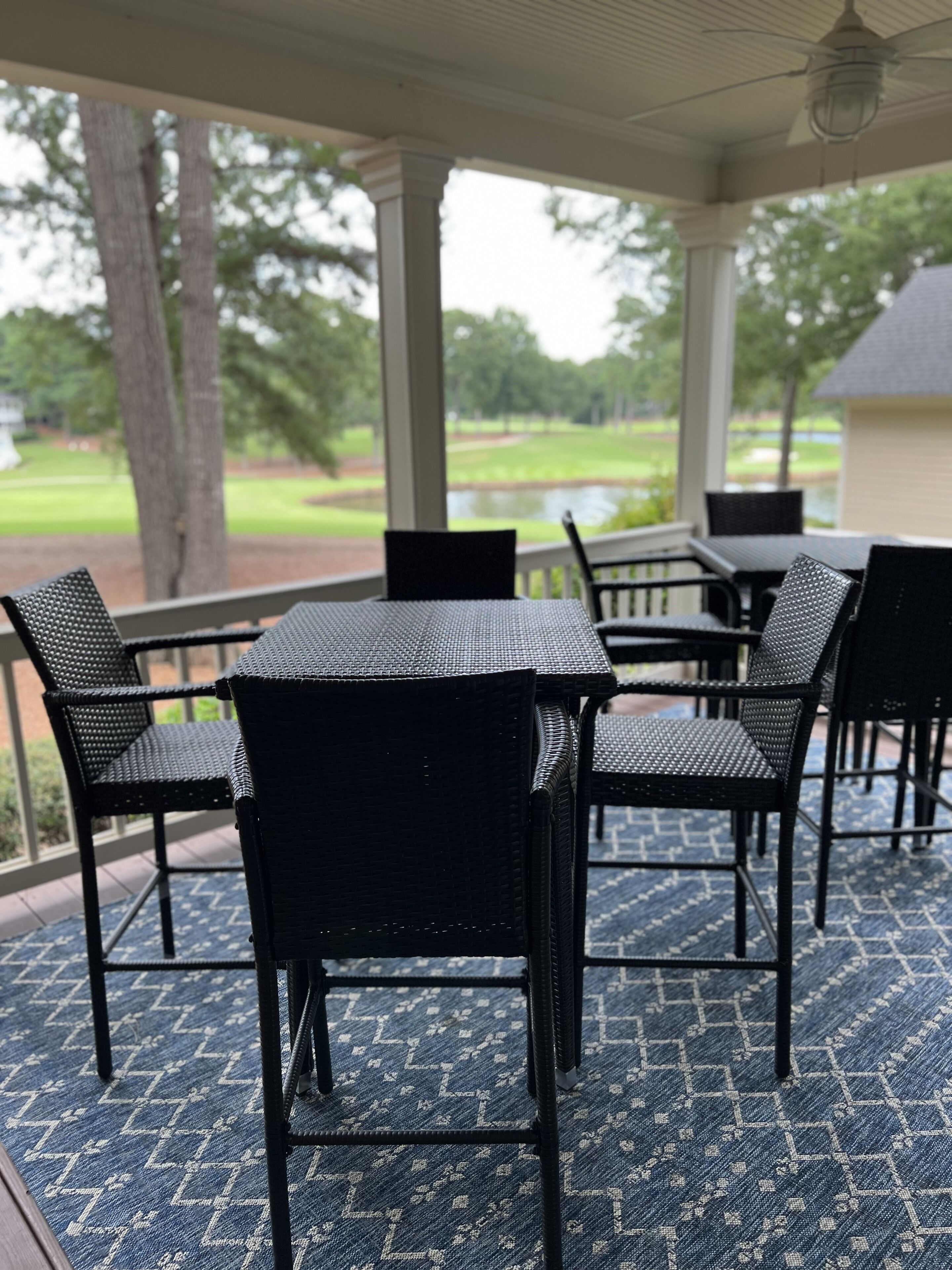 Ein überdachter Patio-Bereich mit Tisch und Stühlen, Blick auf einen Golfplatz und ein Gebäude im Hintergrund.