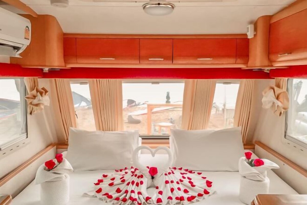 A cozy interior with a bed adorned with rose petals and a heart-shaped decoration, a window with curtains, and a red ceiling.