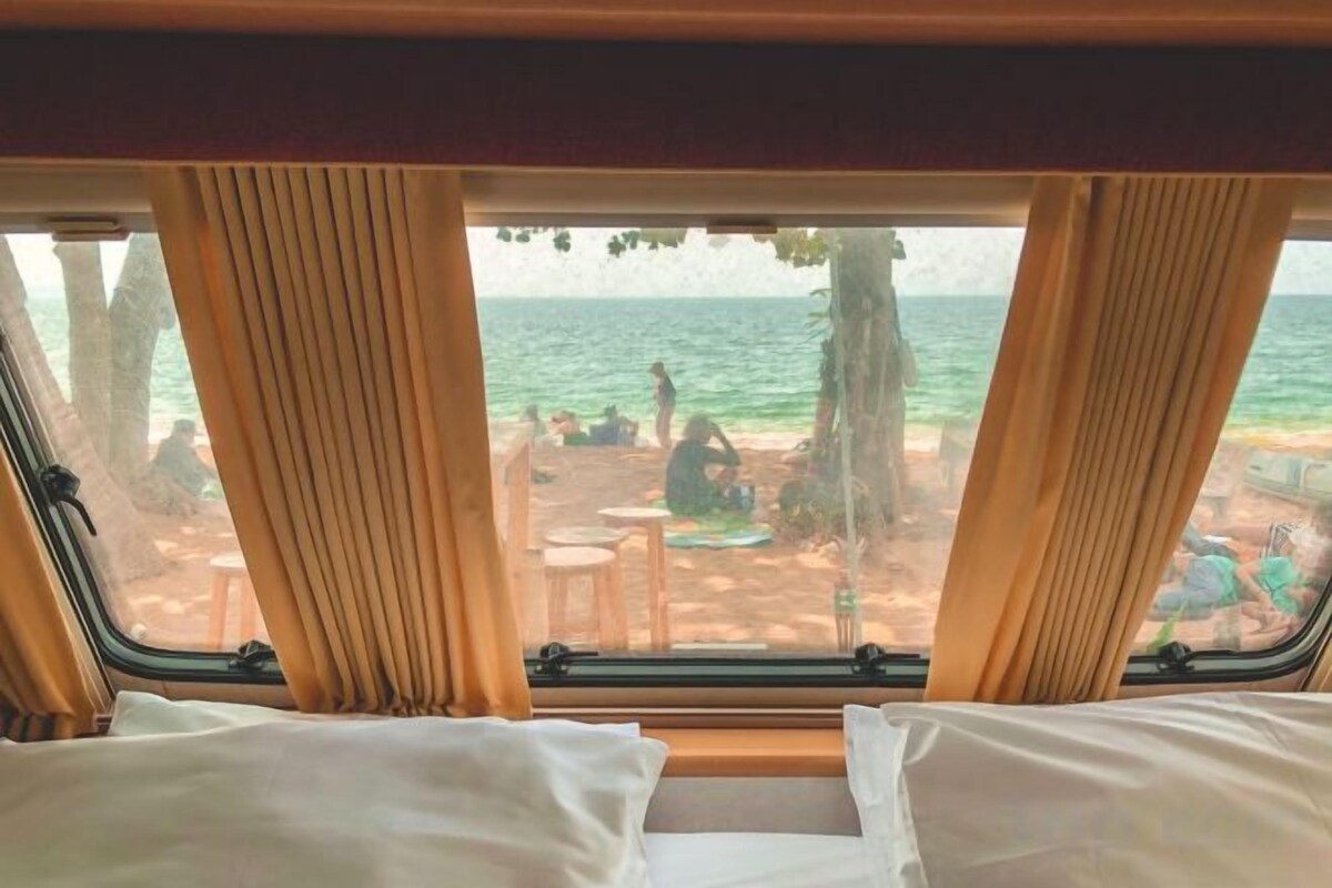 A window view of a beach with a bed and curtains.