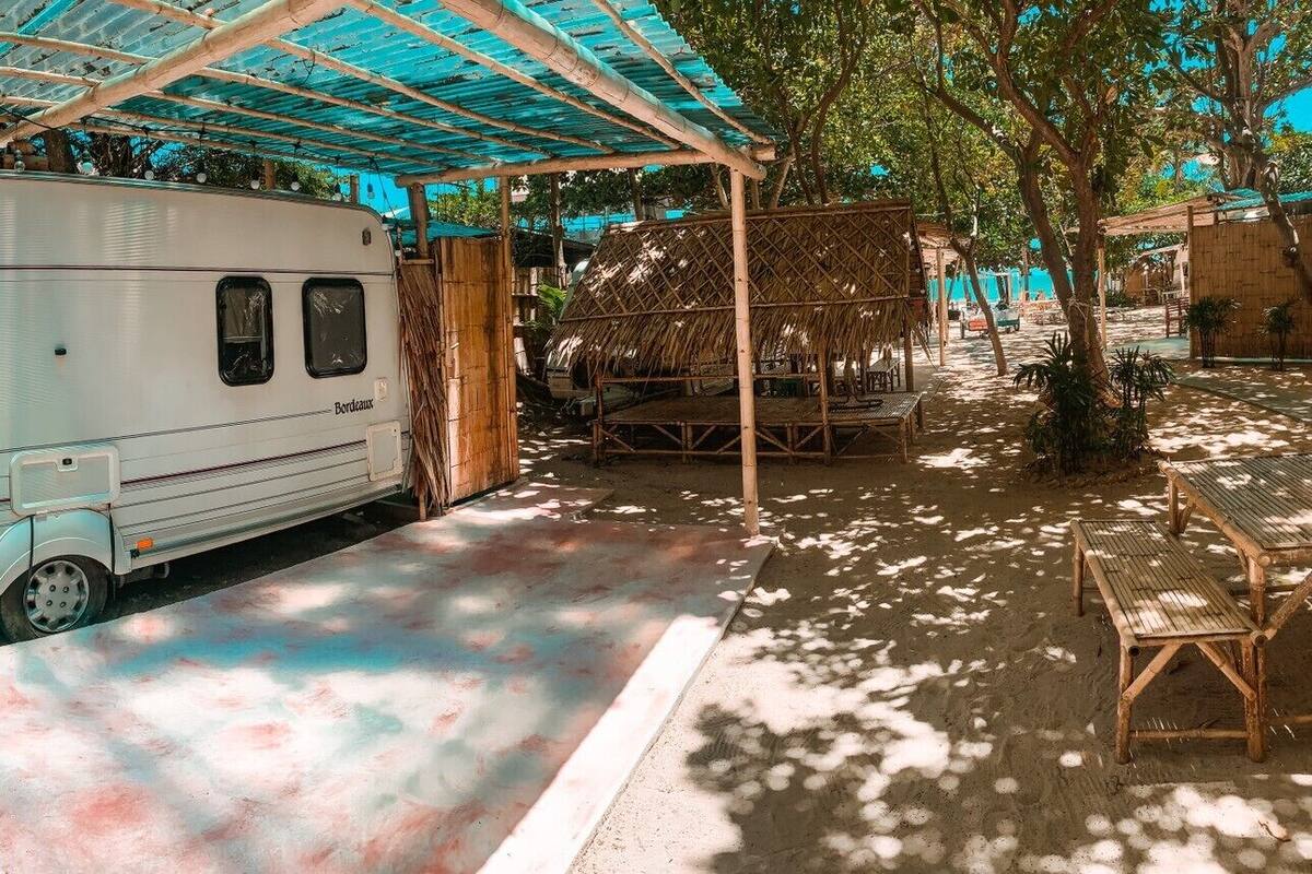 A vintage camper parked under a blue canopy, with a table and chairs nearby.