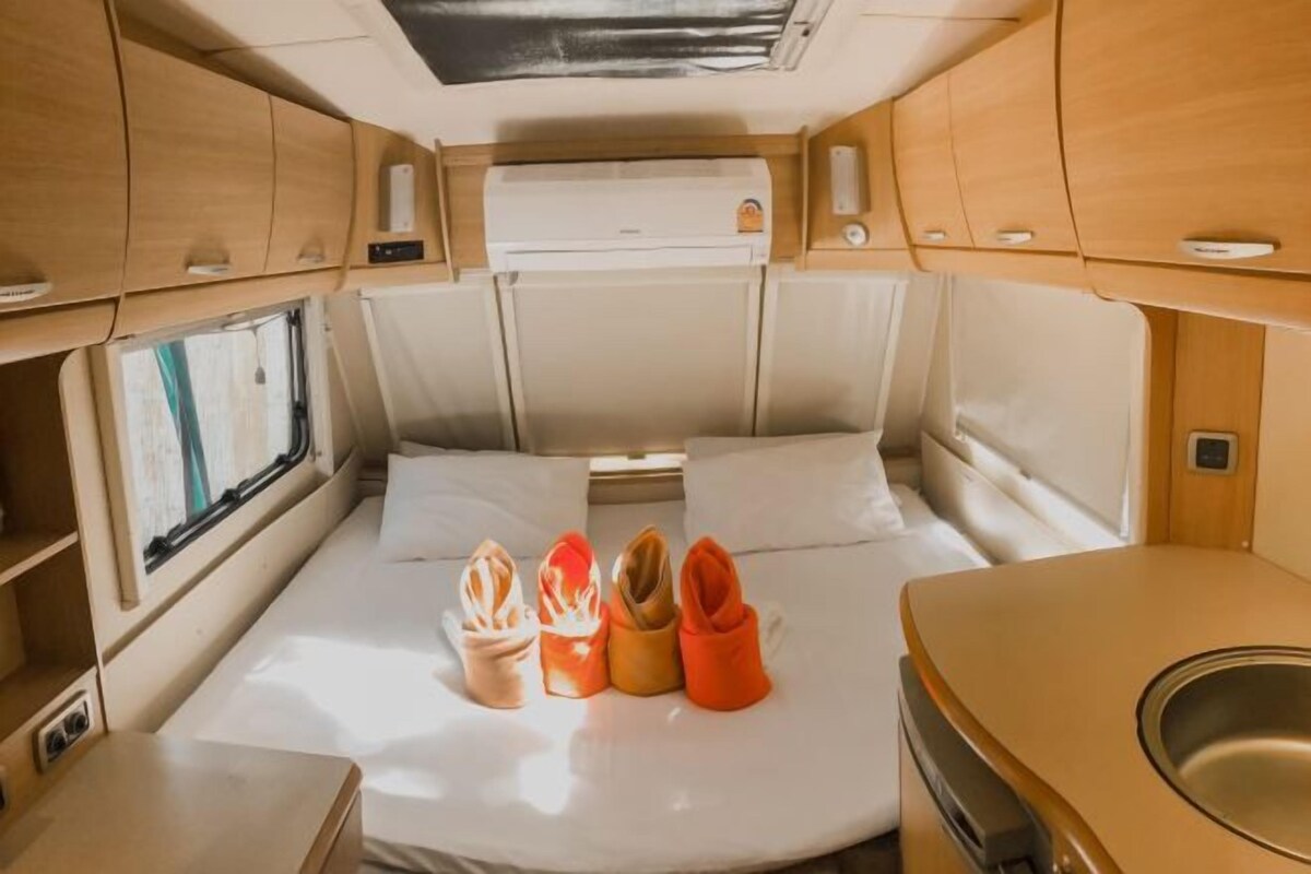 A compact RV interior with a bed, a small kitchenette, and a window.