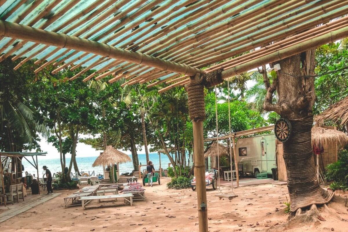 A beachside setting with a wooden table, thatched-roof structures, and a palm tree.