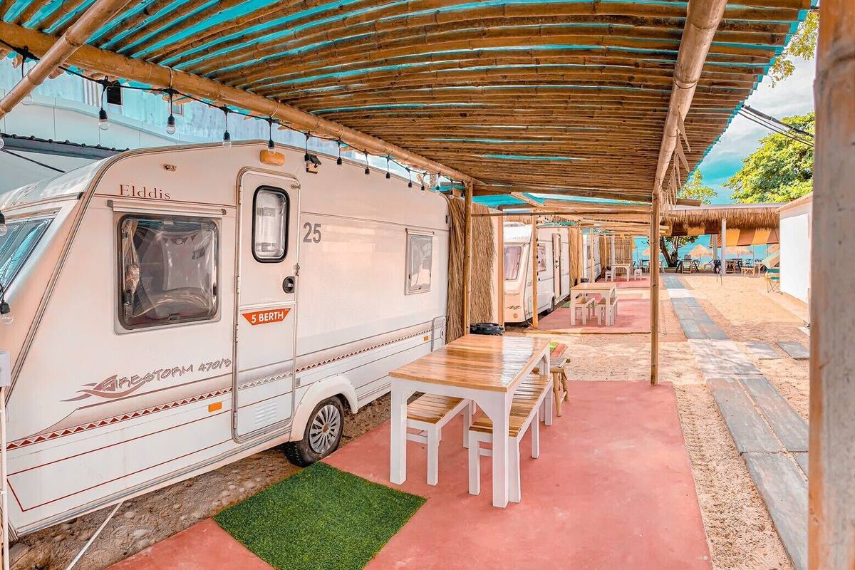 A caravan named 'Elddis' parked under a covered area with a table and chairs.
