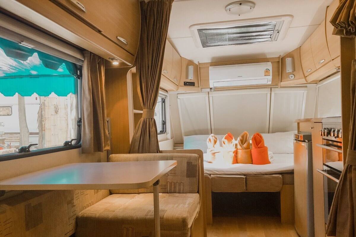 A compact RV interior with a kitchenette, a dining area, and a bed.