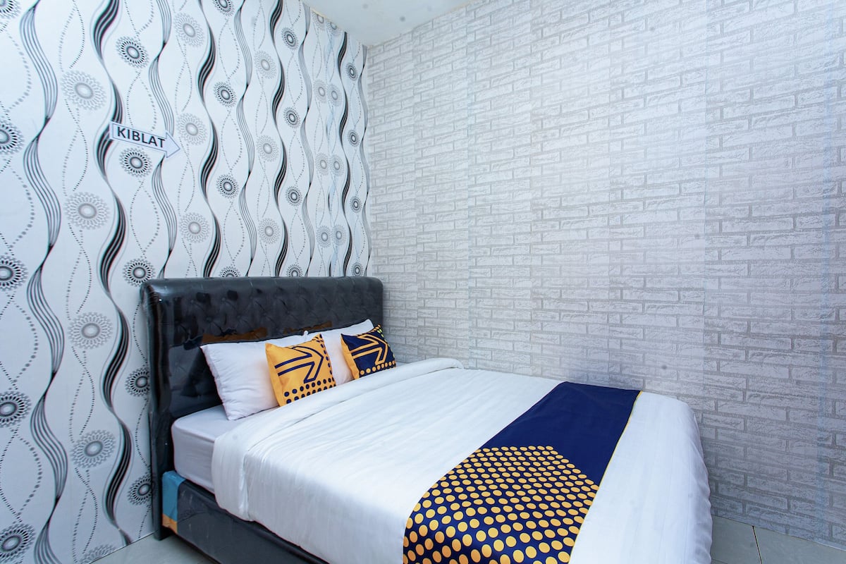 Een net opgemaakt bed met een bedsprei met patroon, een hoofdbord en een muur met een baksteenachtige textuur.