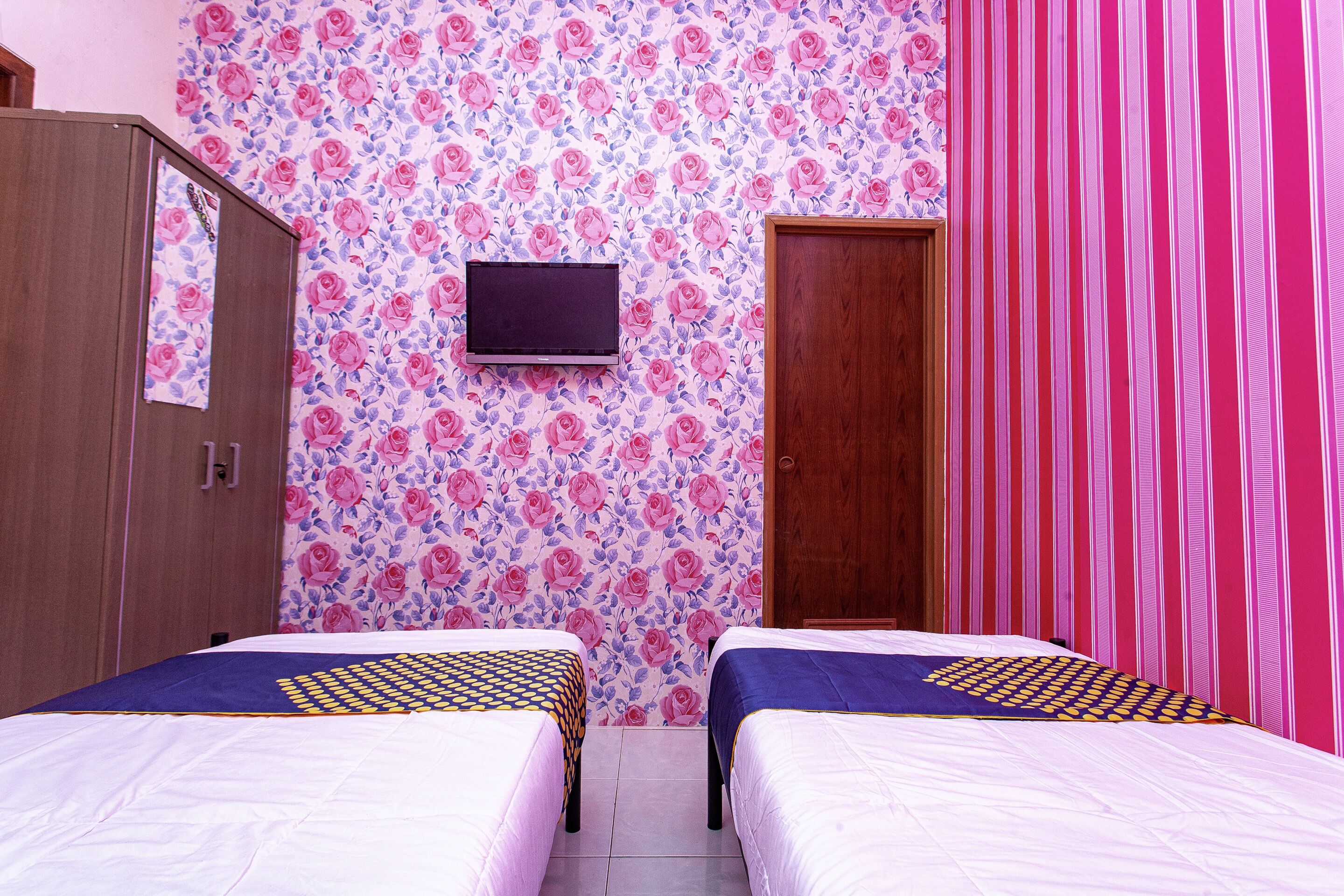 Une chambre avec deux lits, une télévision, une armoire et une porte.