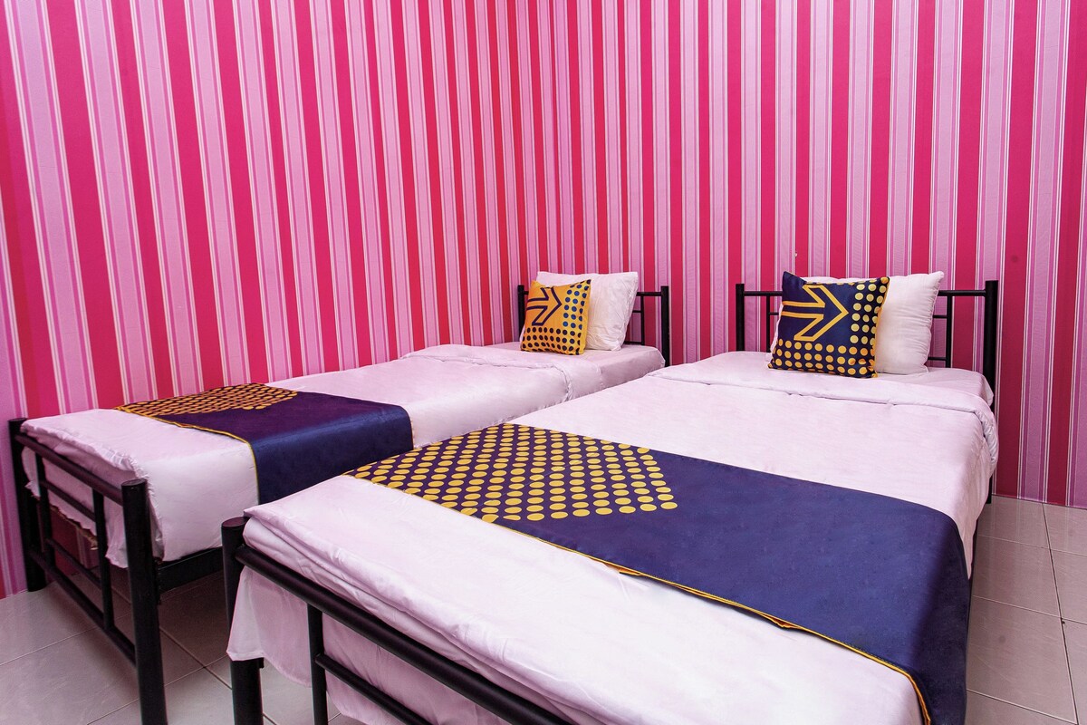 Twee bedden met roze en blauw beddengoed, elk met een geometrisch kussendesign.