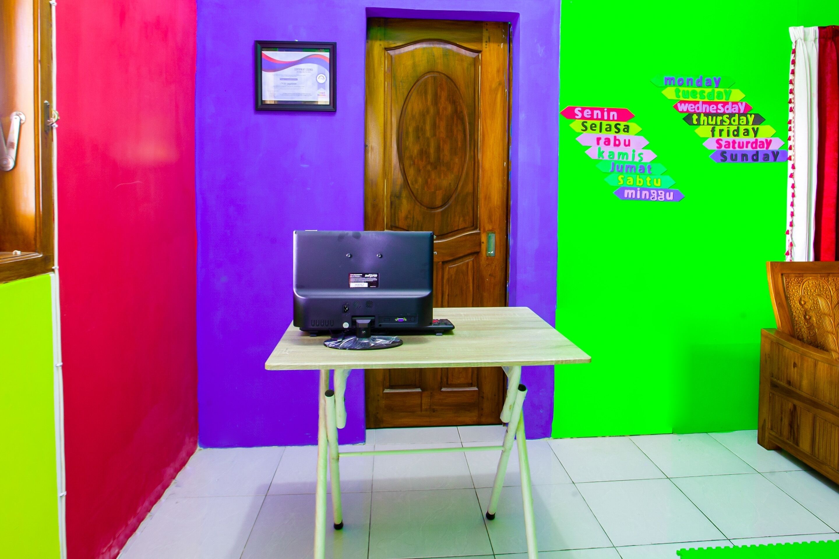 A room with a wooden door, a small table with a computer, and a wall with a colorful word cloud.