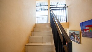 A staircase with beige tiles and a black handrail, leading to a window with a metal roof. - SPOT ON 2875 Kost Pandawa Syariah (Cilacap)
