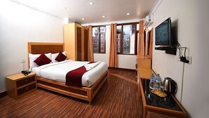 A hotel room with a wooden bed, a nightstand, a TV, and a small table with water bottles and a kettle. - Hotel Pancha Buddha (Kathmandu)