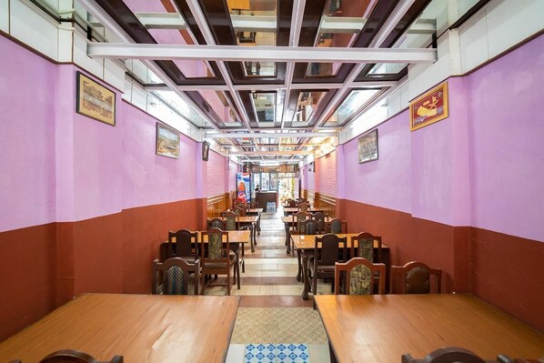 A restaurant with a long counter and multiple tables, featuring a high ceiling with exposed beams and a tiled floor.