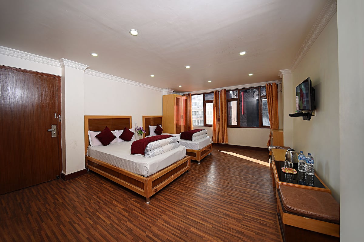 A hotel room with two beds, a wooden floor, a TV, and a small table with water bottles.