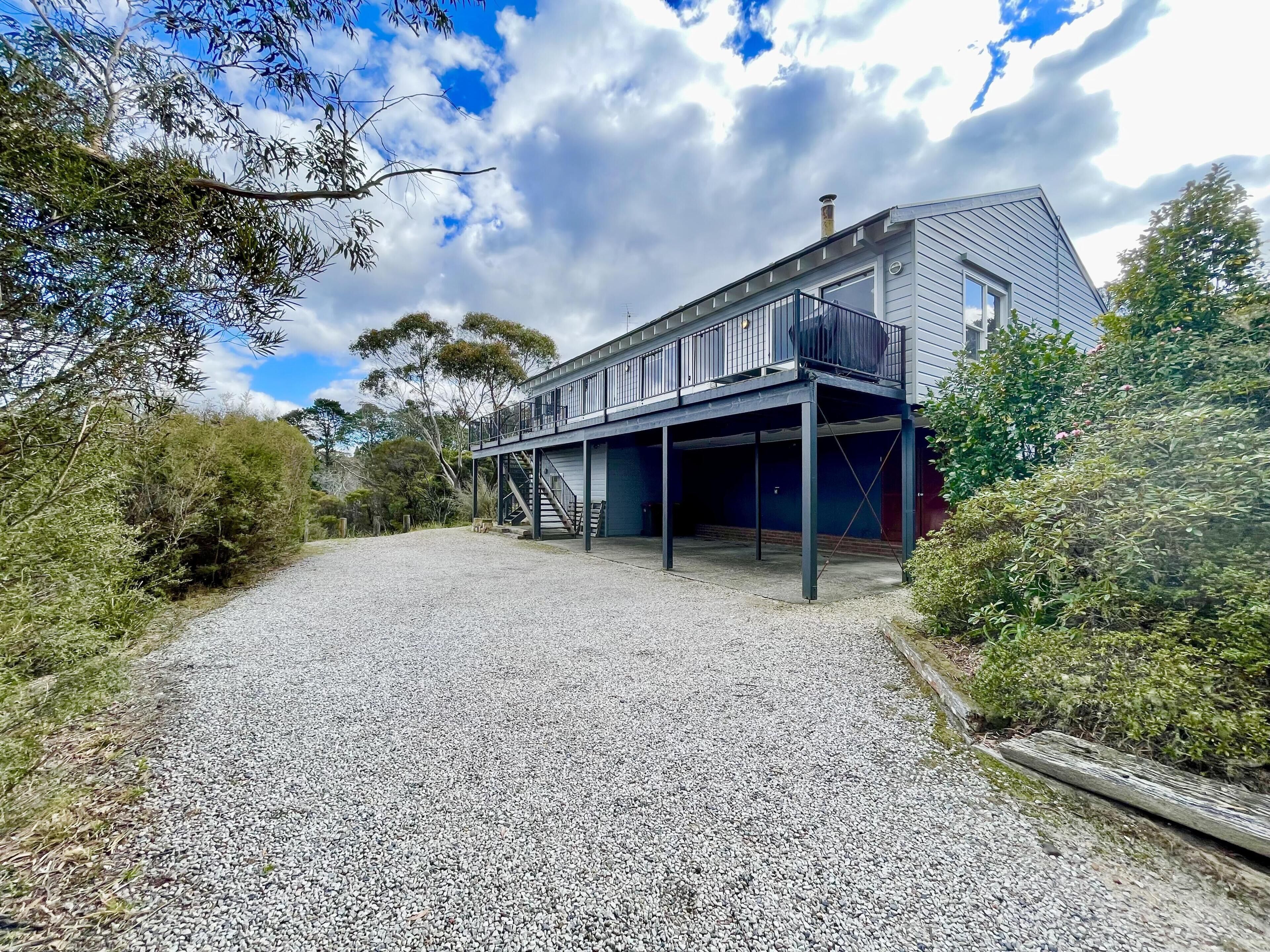 A two-story house with a covered outdoor area and a gravel driveway.