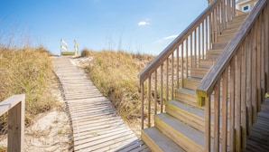 A wooden boardwalk leading to a beach area with a staircase on the right.