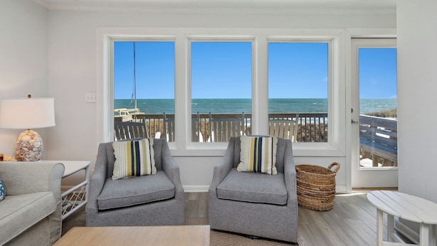 A room with two grey armchairs, a small table, and a view of the ocean through large windows.