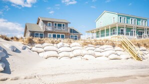 A beachfront property with two houses, one with a balcony and the other with a porch, surrounded by sandbags.