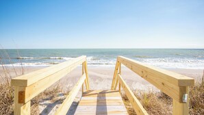 A wooden boardwalk leading to a beach with waves in the background.