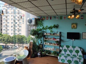 A room with a view of a cityscape, a bookshelf with various items, and a television on the wall.