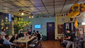A restaurant with a long communal table, ceiling fans, and a TV screen. - Foshan school age Youth Hostel (Foshan)