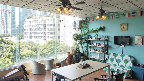 A room with a large window, ceiling fans, a table with chairs, a bookshelf, and a TV. - Foshan school age Youth Hostel (Foshan)